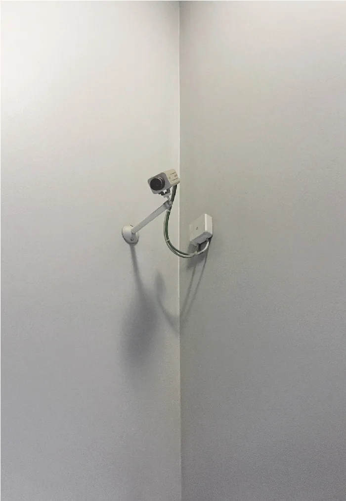 Camera on a curved arm in the corner of a white room, casting a soft shadow