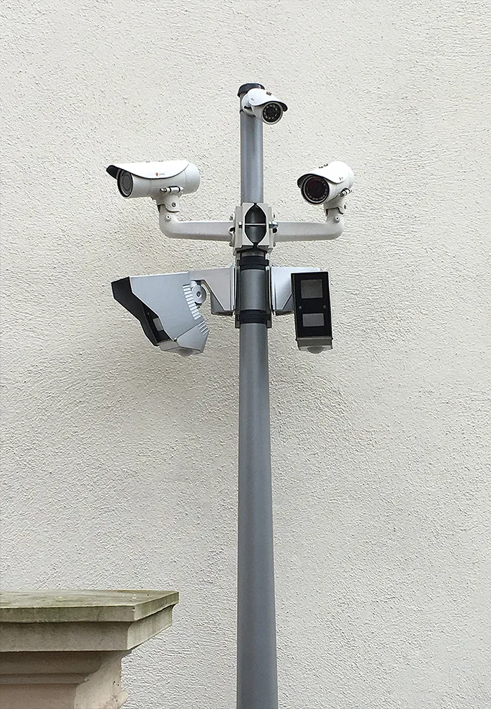 Pole with several cameras and a sensor box in front of a white wall