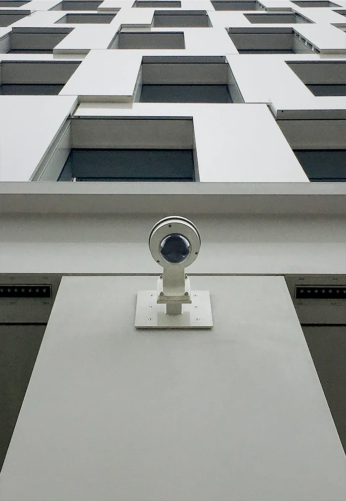 Camera on a white ledge in front of a building with staggered square windows