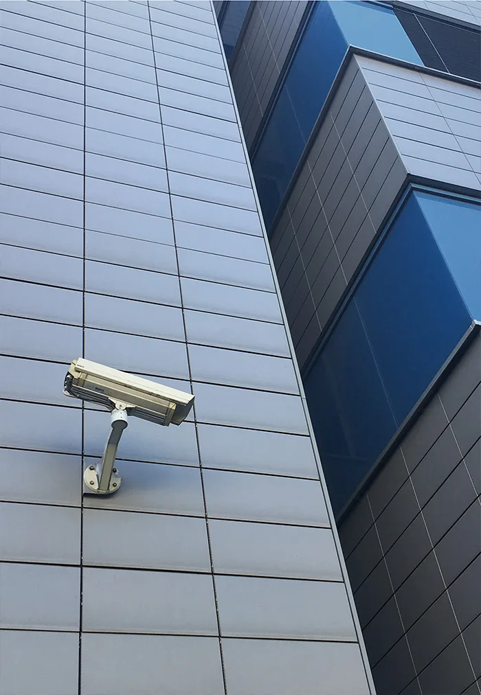 Camera on a grey-blue metal facade next to a projecting blue glass section