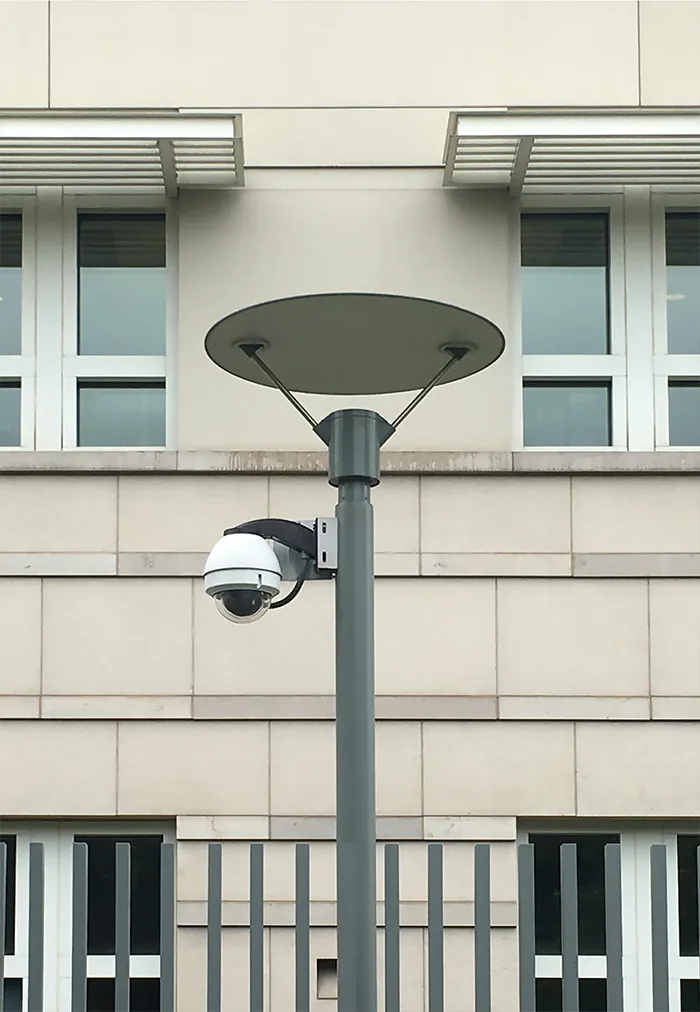 Dome camera on a lamp post in front of a pale stone building with barred windows