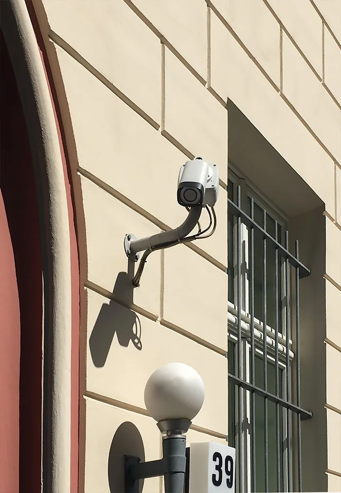 Camera on an arm beside a barred window and a globe lamp on a sandstone wall