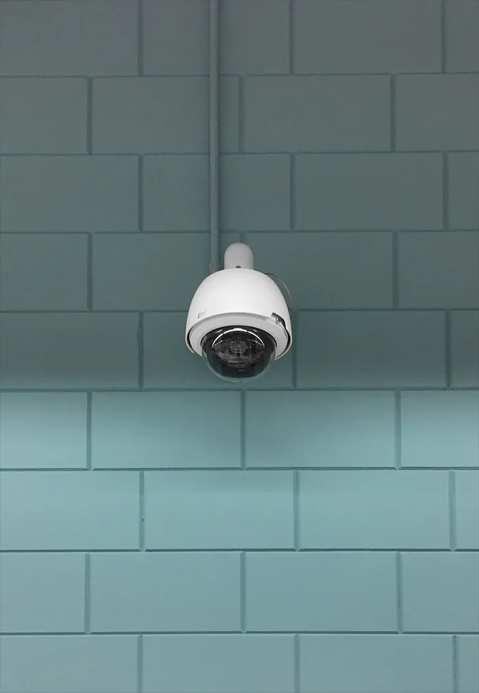 White dome camera hanging from a pipe in front of a turquoise tiled wall