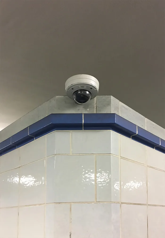 Dome camera on a building corner clad in cream tiles with a blue band