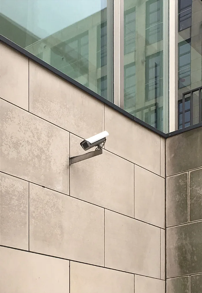 Camera on a beige stone wall below a band of glass windows