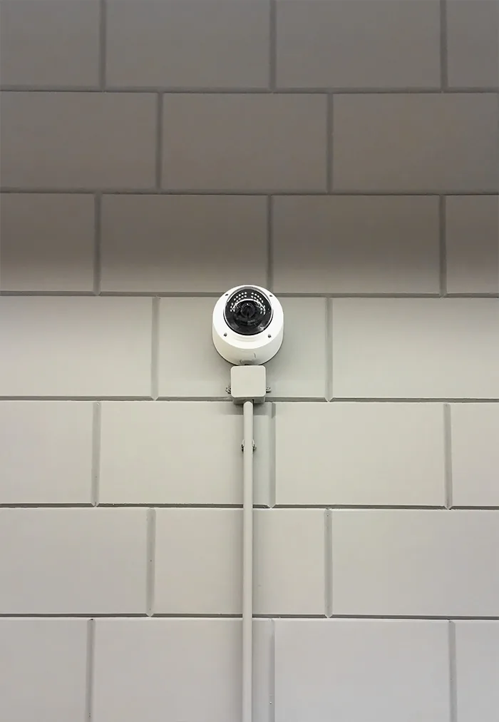 Round camera on a wall of pale stone blocks, its cable running down