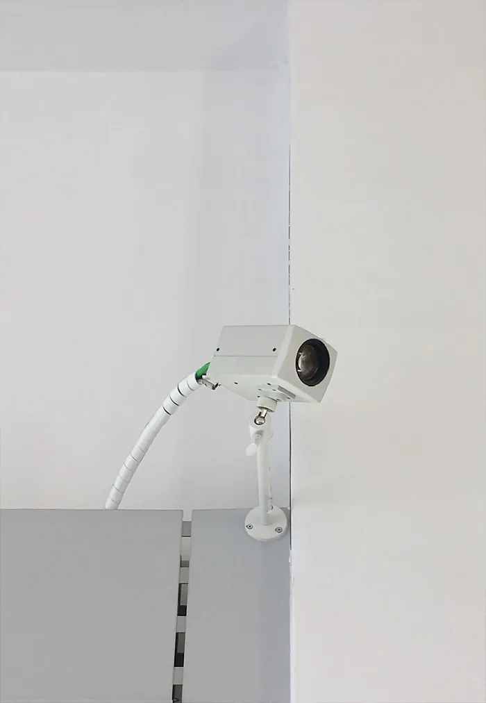 Box camera with a white cable mounted in a white corner