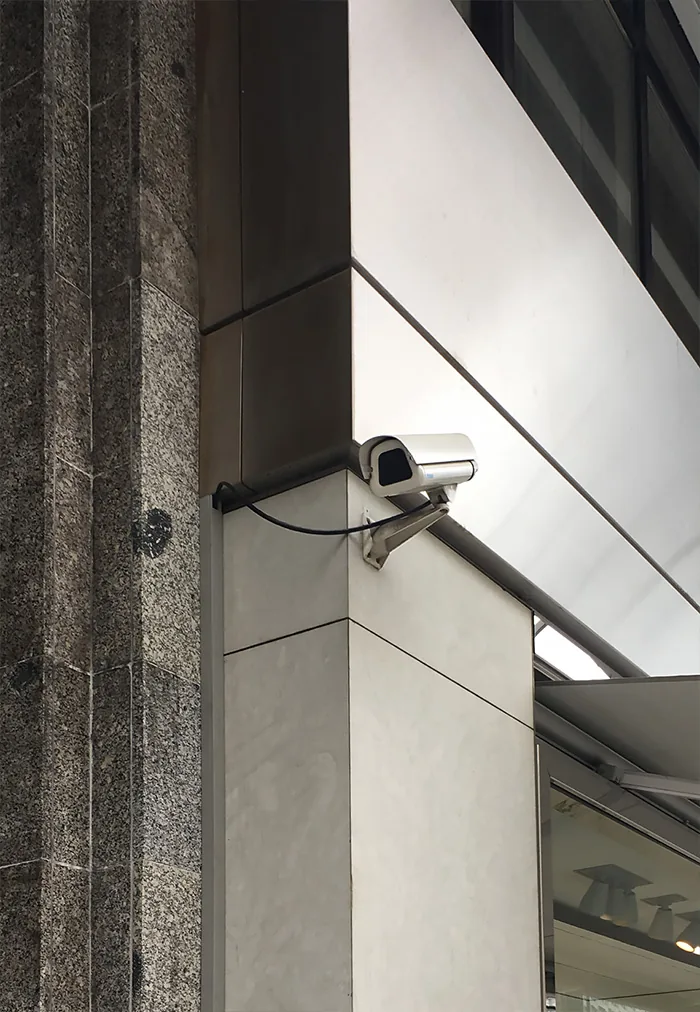 Camera on a bracket at the corner of a white building beside a granite column