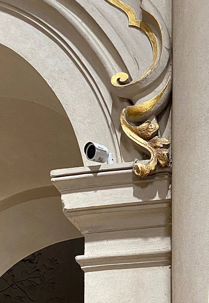 Small camera tucked under the gilded ornament of a stone arch