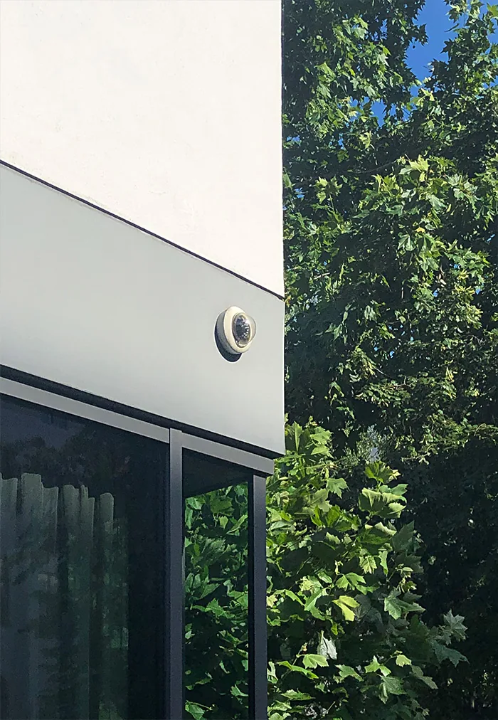 Small dome camera on the edge of a white building next to green leaves