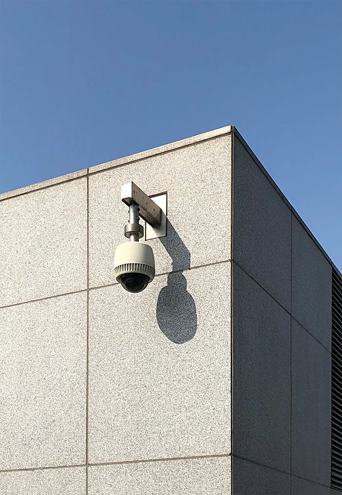 Dome camera on a bracket at the top of a stone building against a blue sky