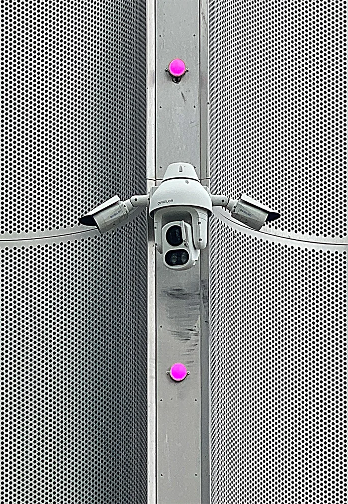 Multi-lens camera on a pole between perforated metal panels